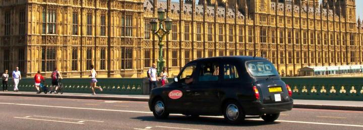 Stock image of a ComCab black cab whizzing past Parliament